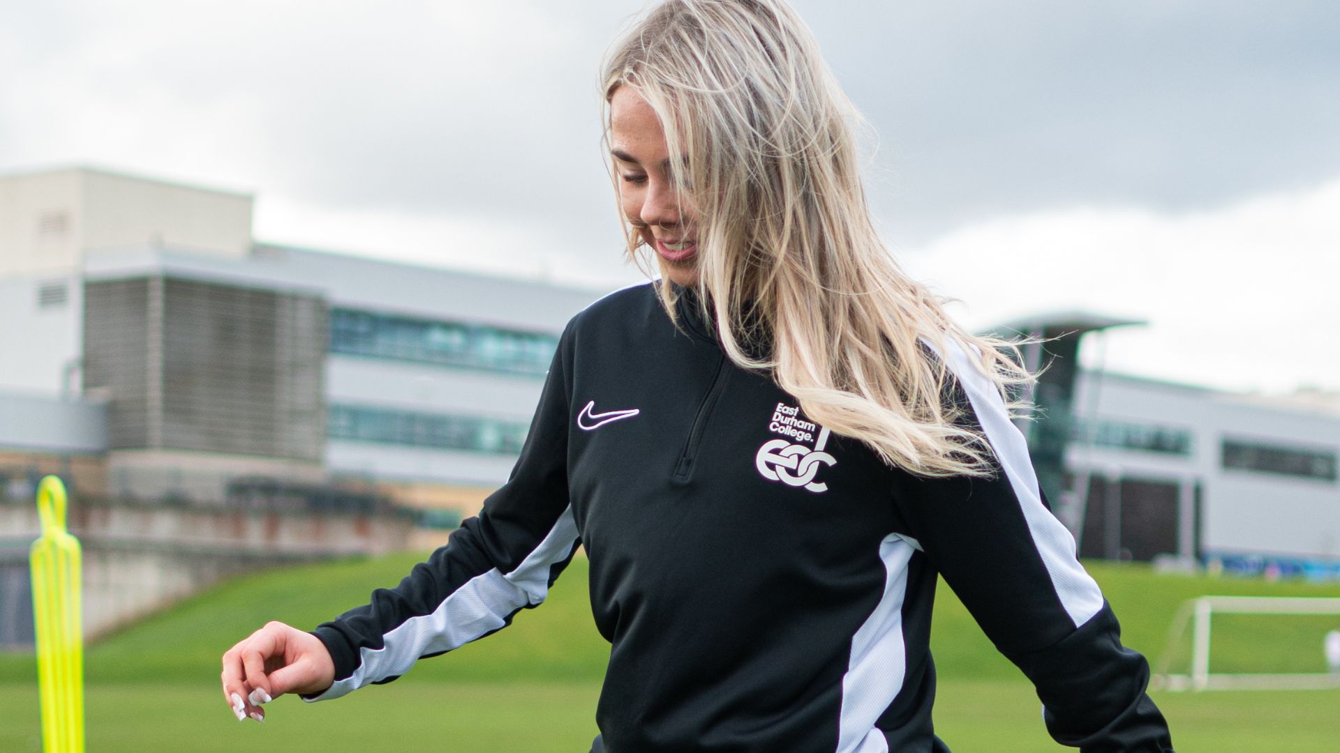 Smiling female student playing football outside of East Durham College