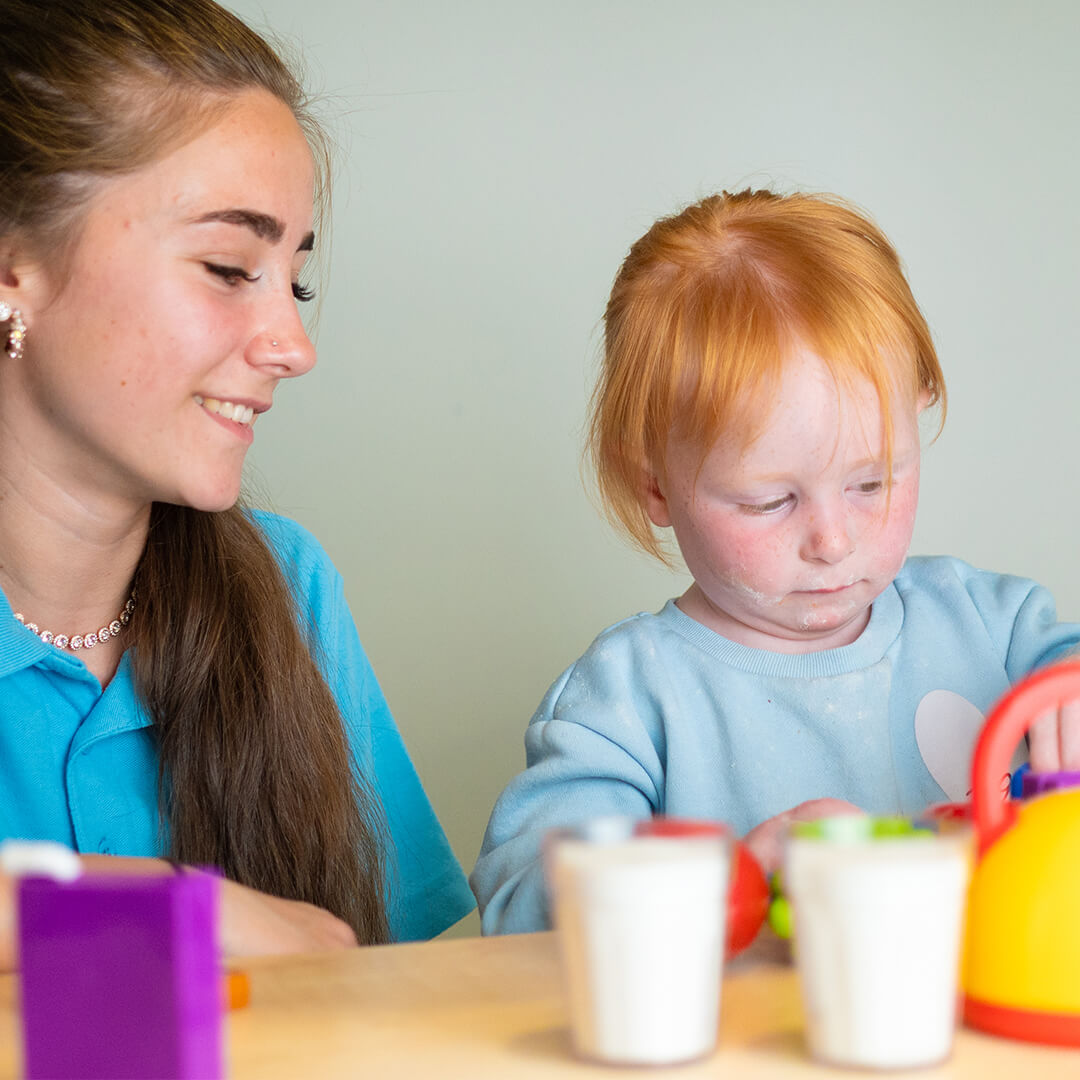 Young woman smiling at young child playing.