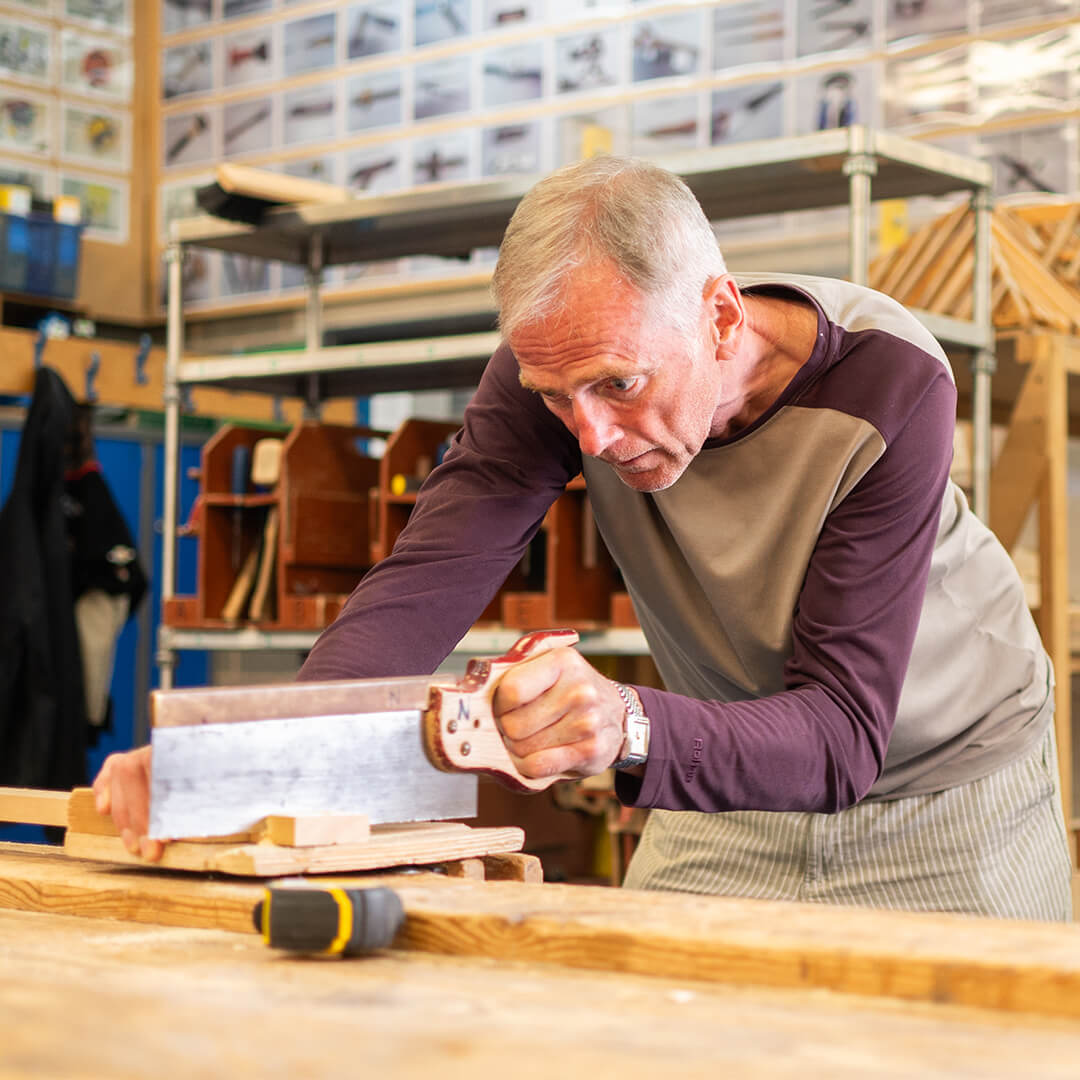 Man leaning over bench sawing block of wood.