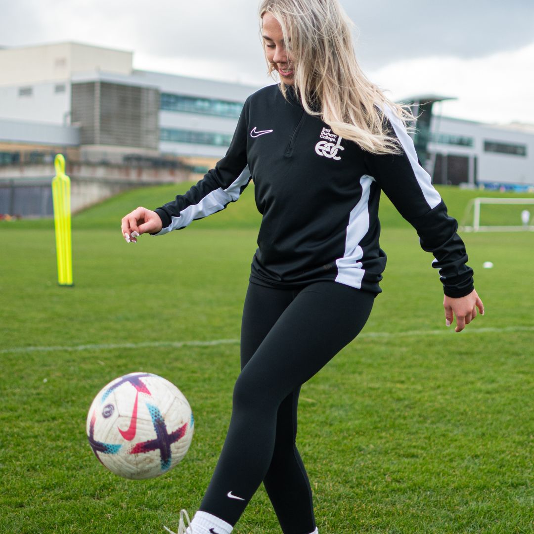 Smiling female student playing football outside of East Durham College