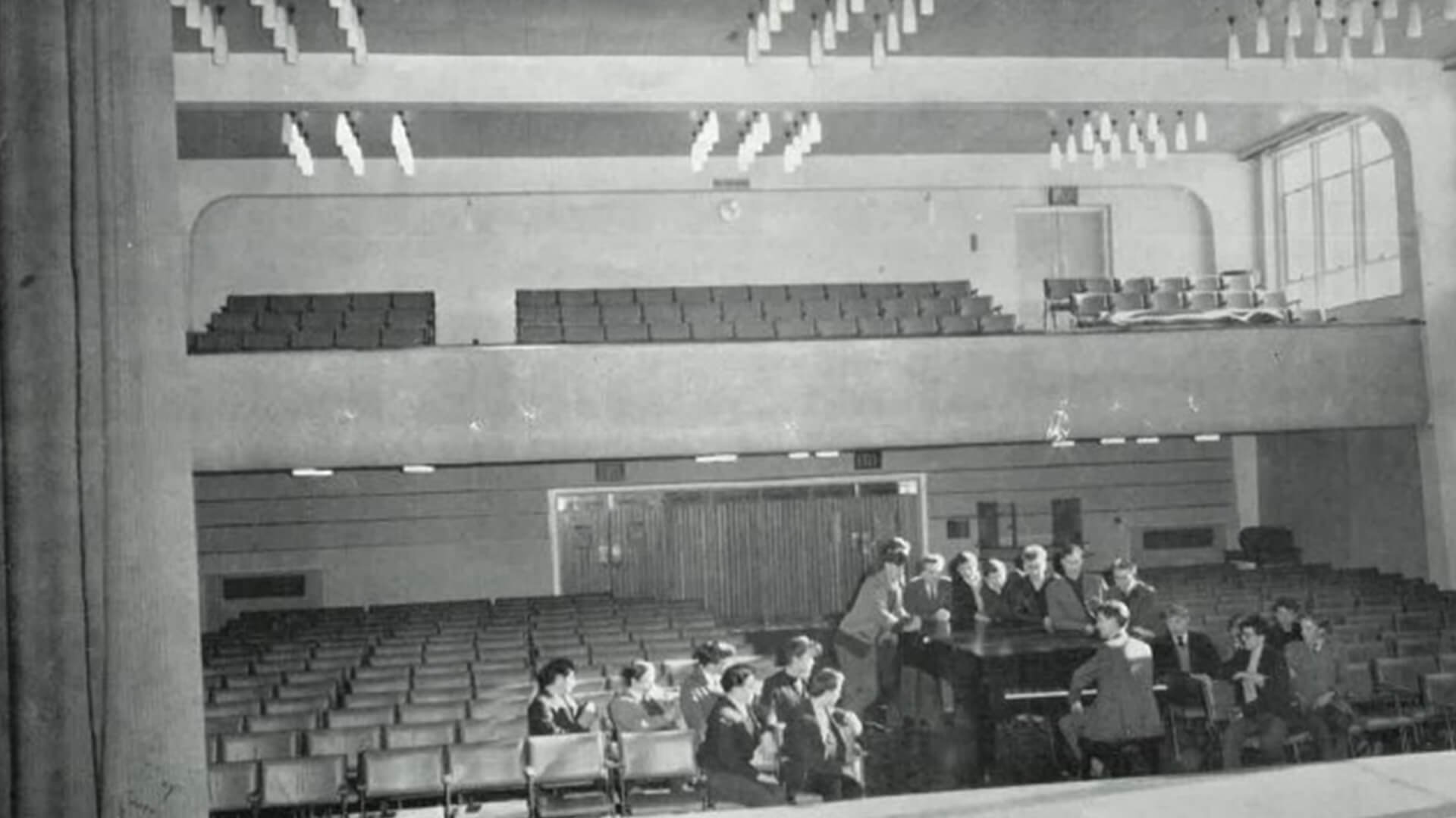 A black and white photo of the Easington College theatre hall with group singing and playing piano